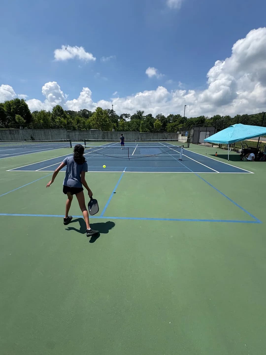 Young players rallying across blue and green outdoor pickleball courts