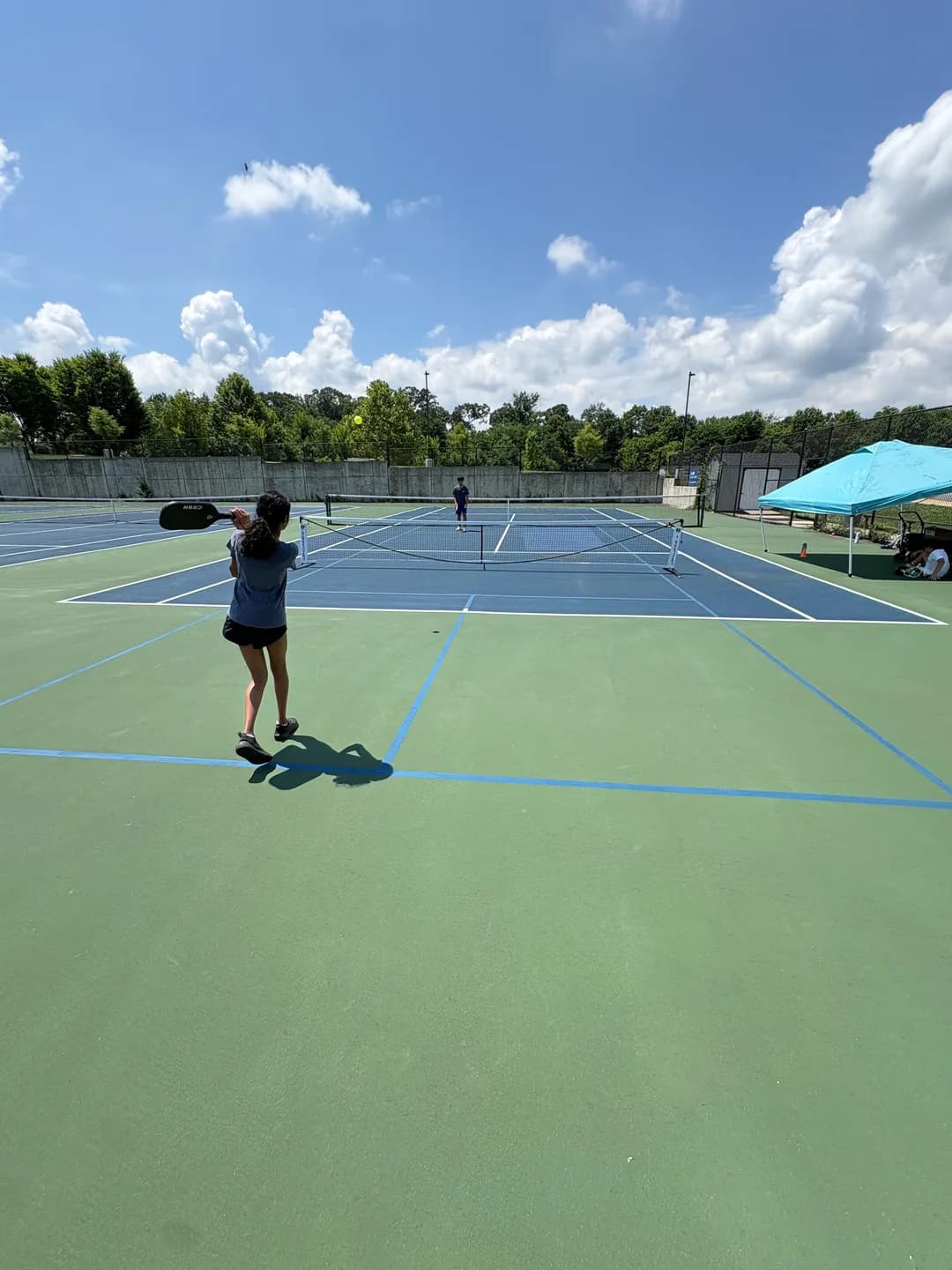Young players rallying across blue and green outdoor pickleball courts