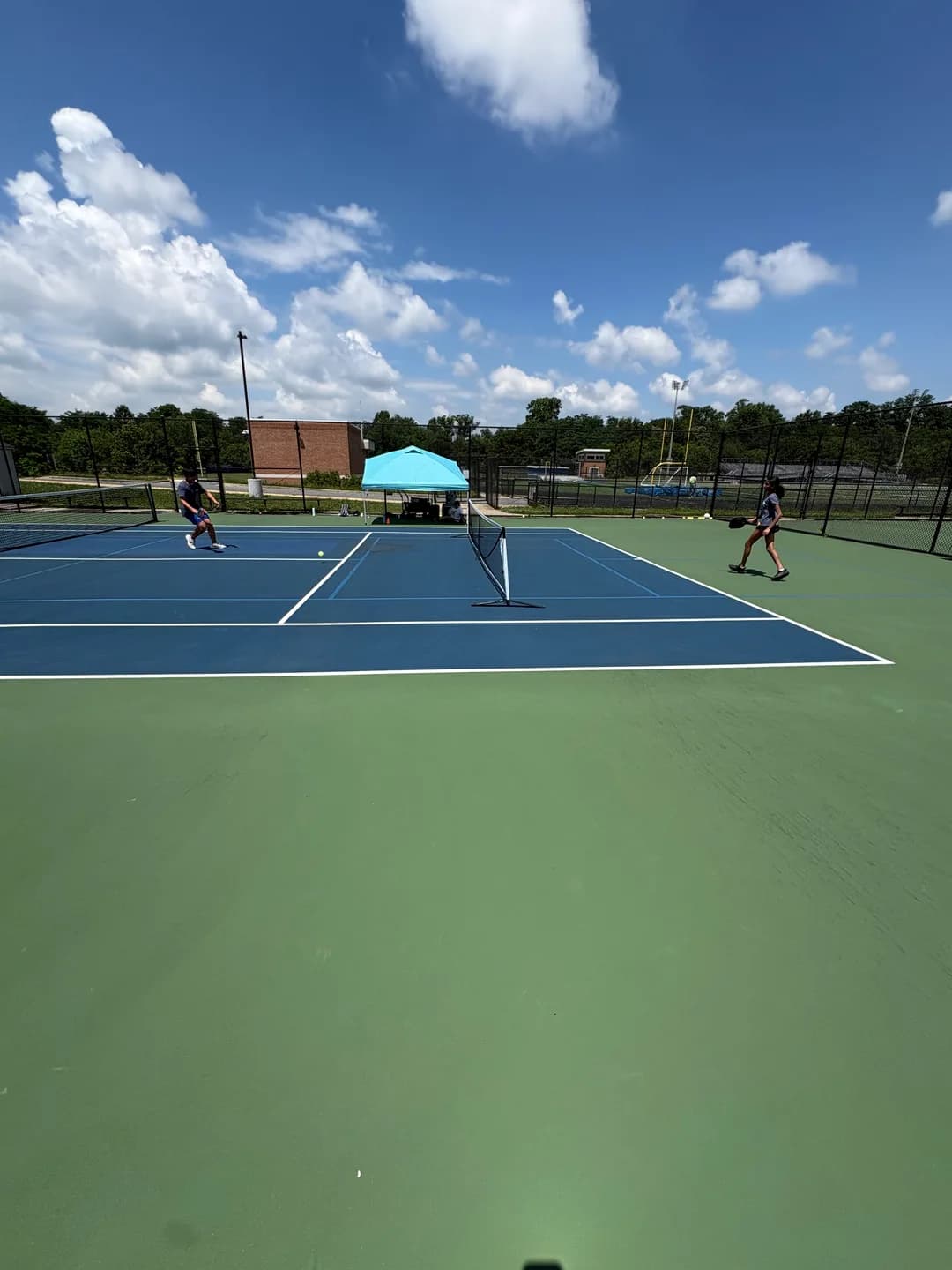 Young players rallying across blue and green outdoor pickleball courts