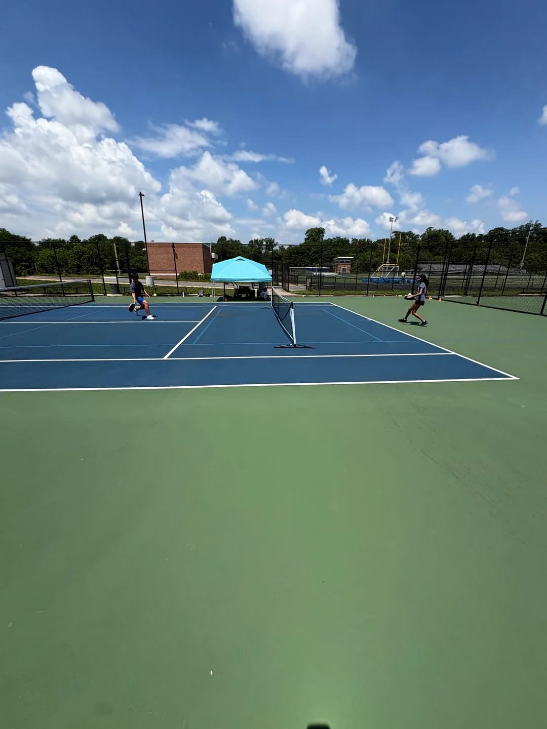 Young players rallying across blue and green outdoor pickleball courts