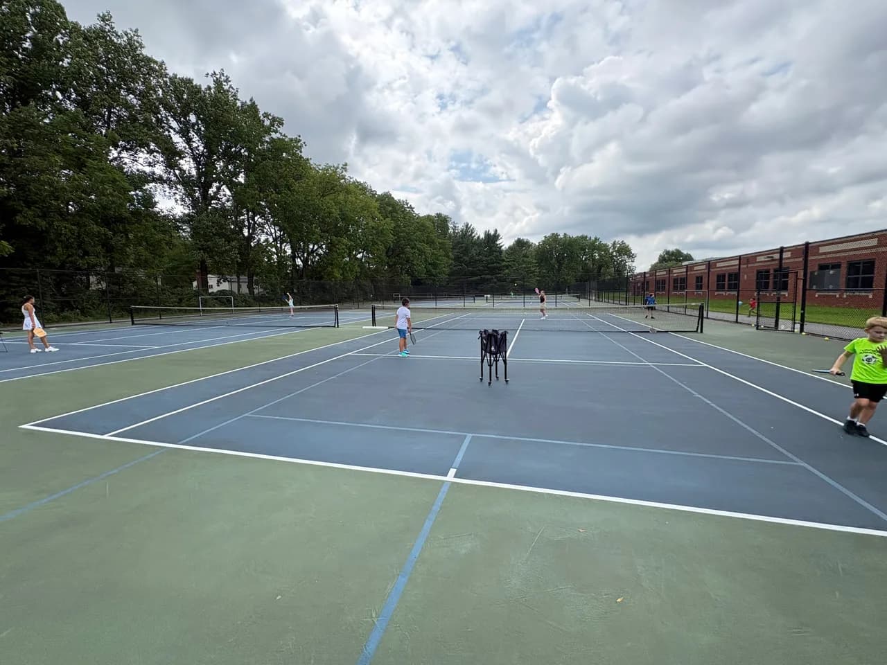 Young players rallying across blue and green outdoor pickleball courts