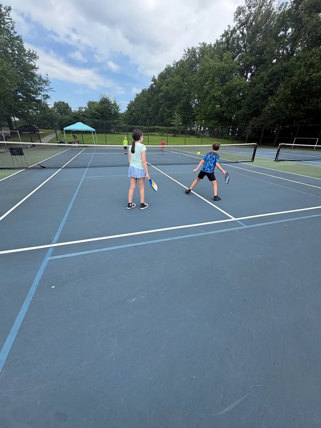 Young players with paddles on a blue outdoor pickleball court