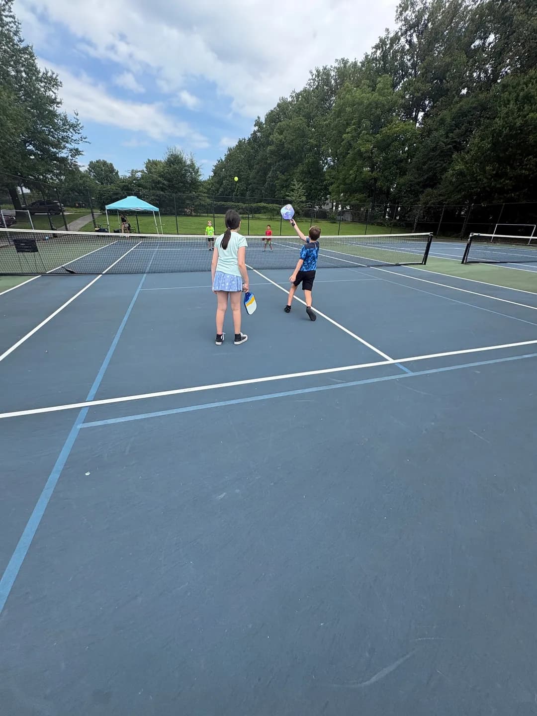 Young players with paddles on a blue outdoor pickleball court