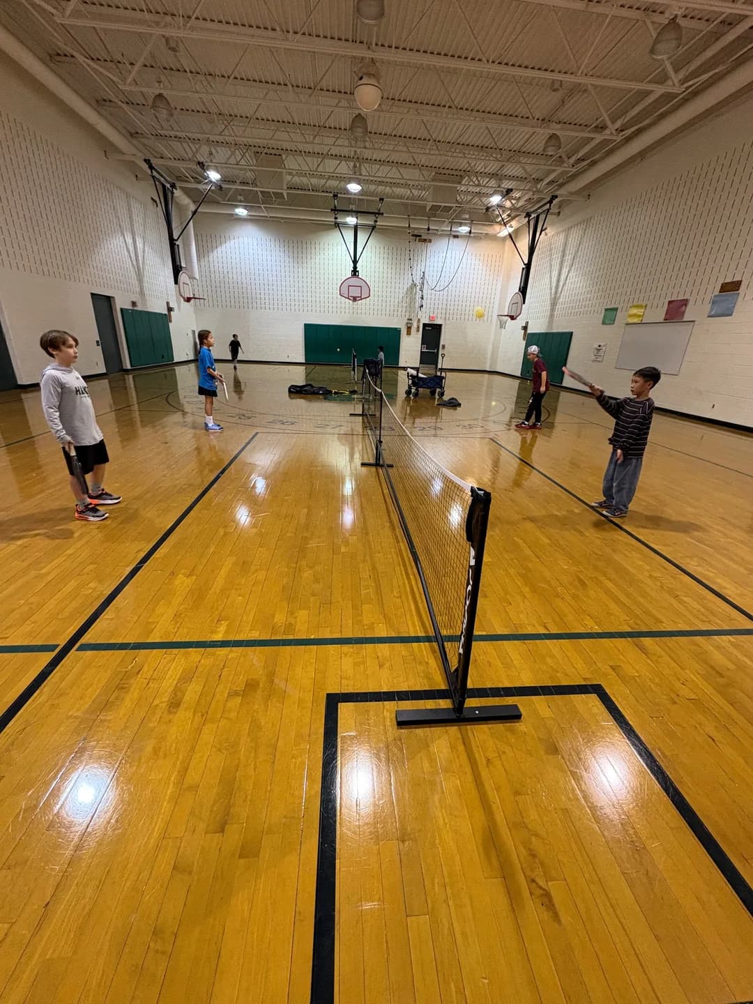 Young players on both sides of a pickleball net inside a gym