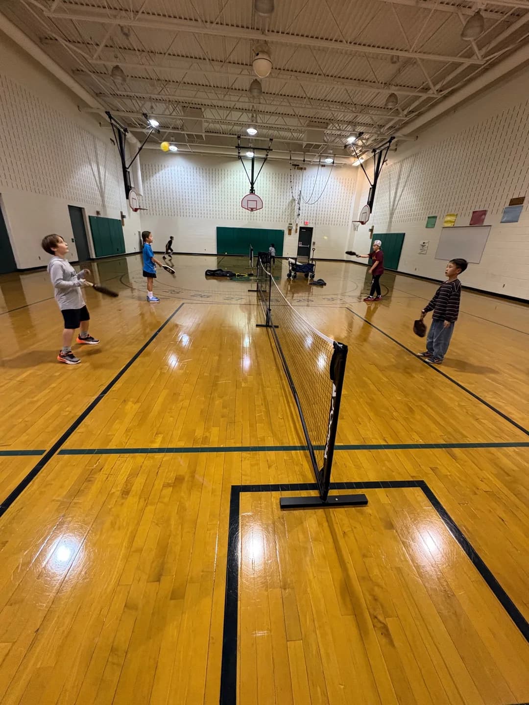 Young players on both sides of a pickleball net inside a gym