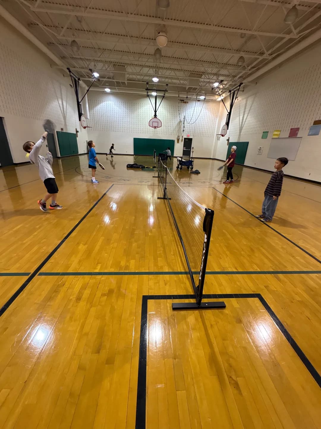 Young players on both sides of a pickleball net inside a gym