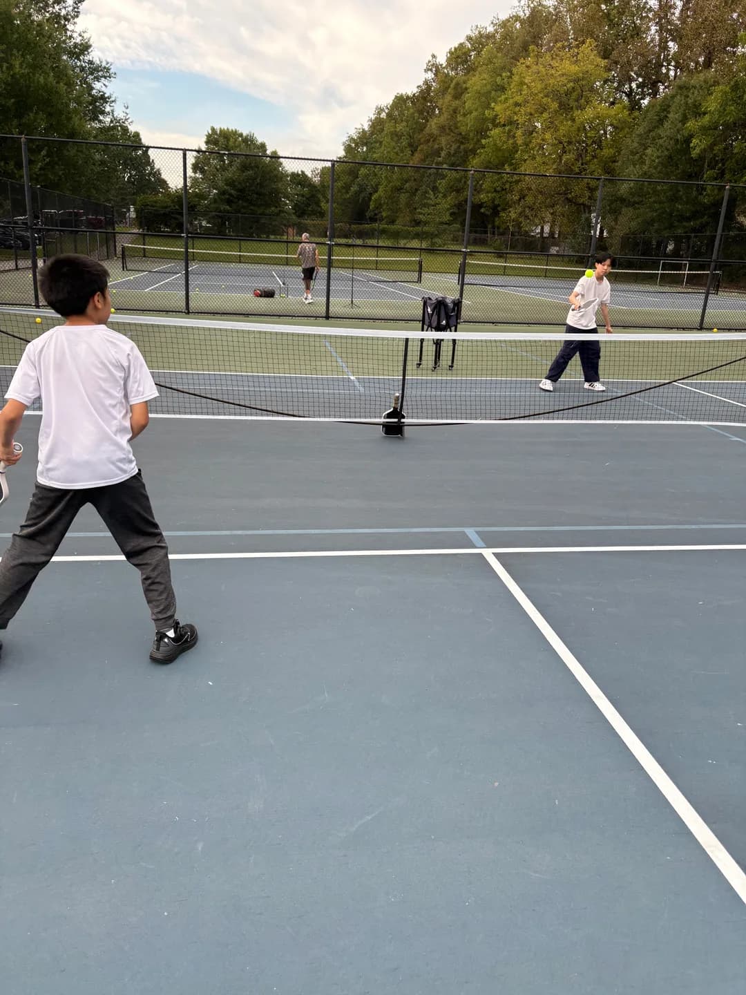 Young players rallying on outdoor courts bordered by trees