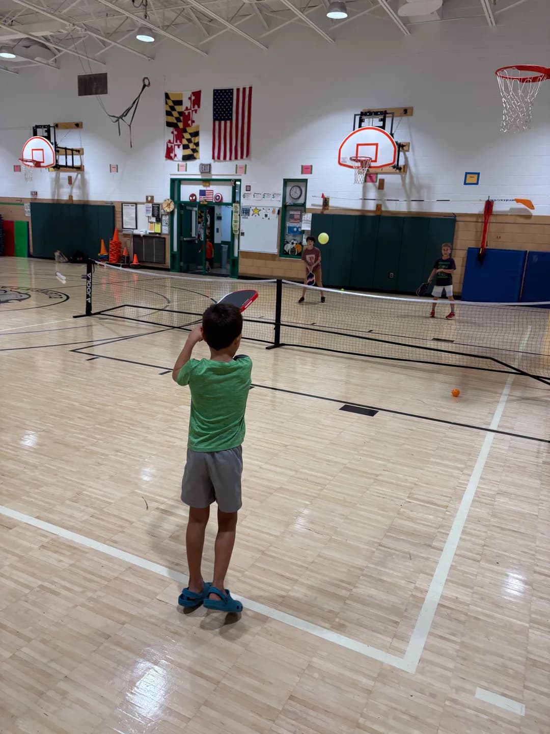 Young players with paddles playing pickleball across a portable net in a school gym