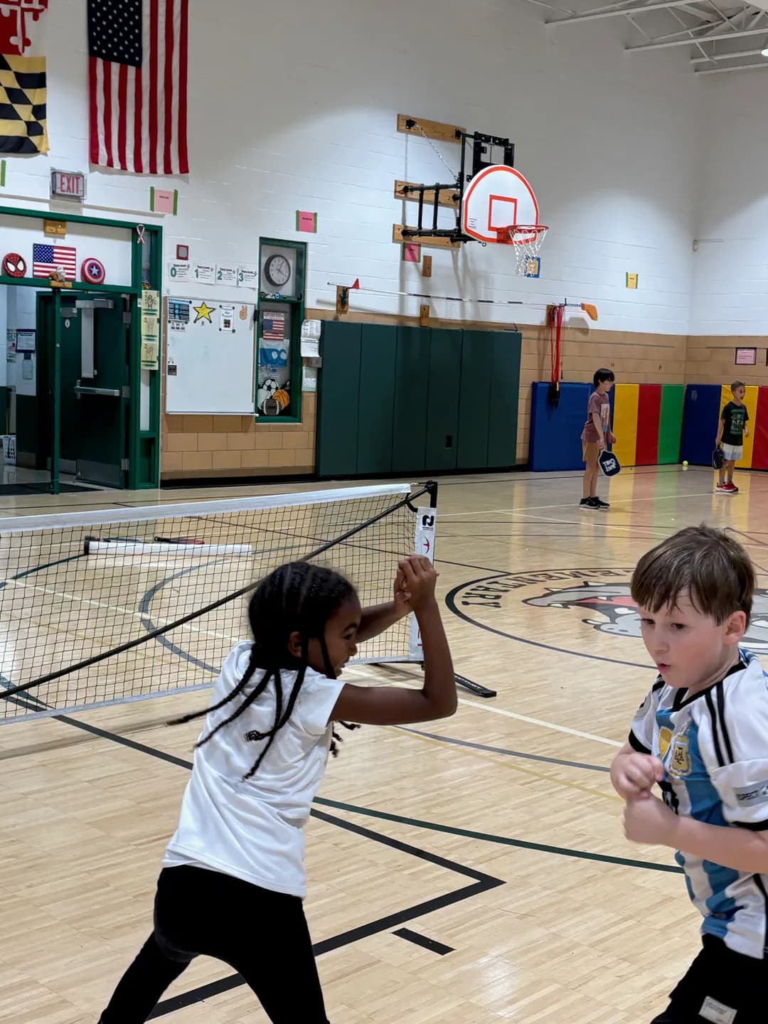 Two young players standing together beside a net in a school gym
