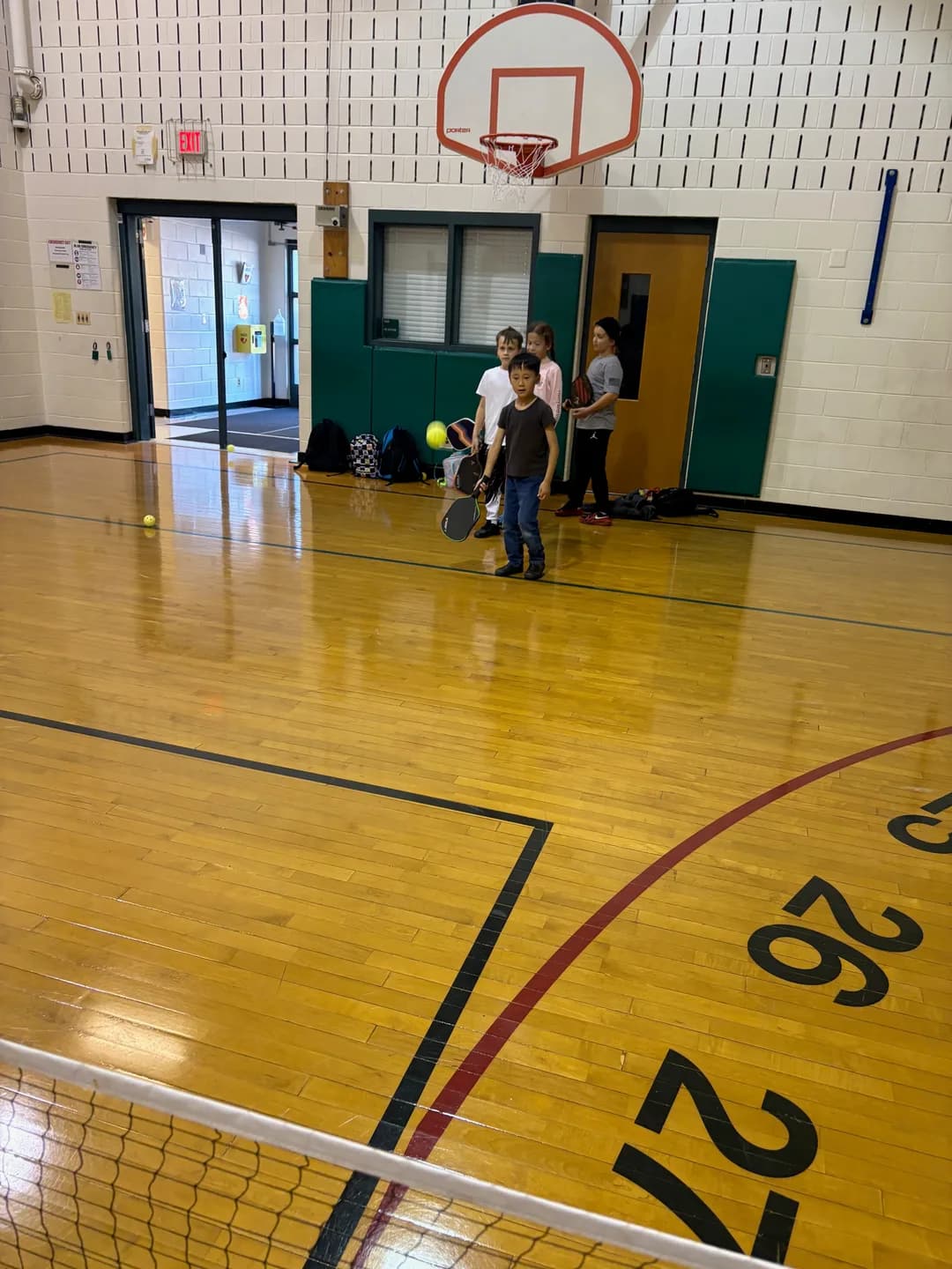 Young players gathered with paddles at the edge of a school gym