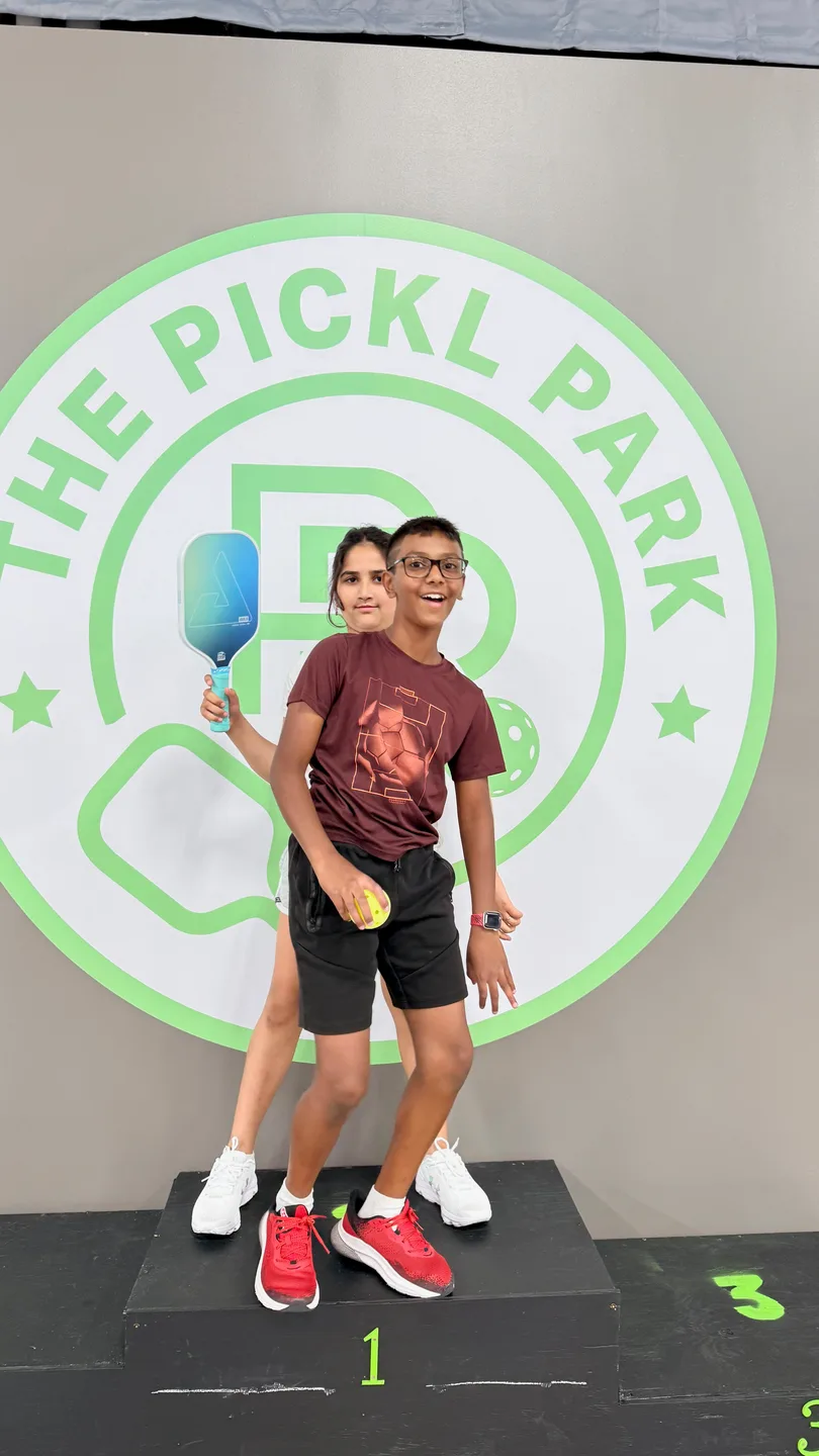 Young players holding paddles beside a Pickl Park wall graphic