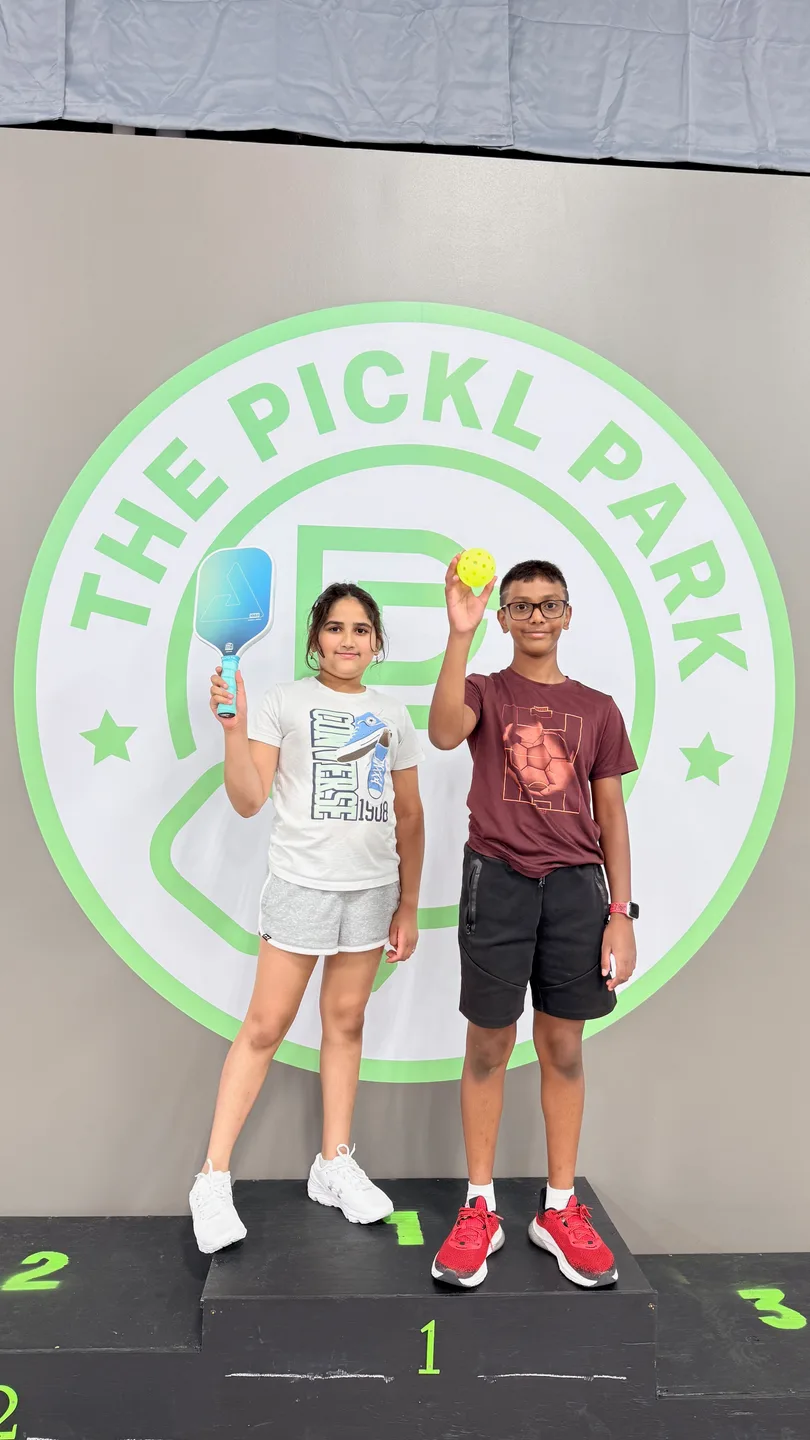 Young players holding paddles beside a Pickl Park wall graphic