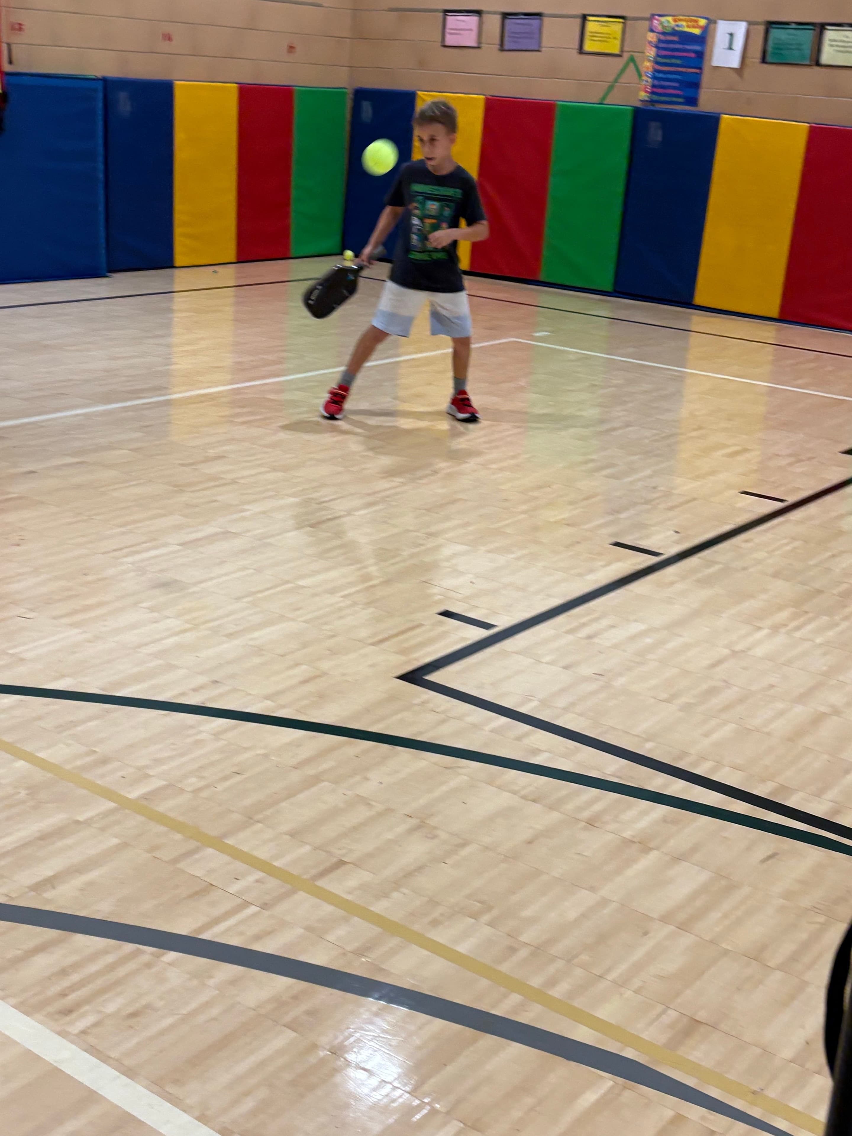 A young player returning a ball in a gym