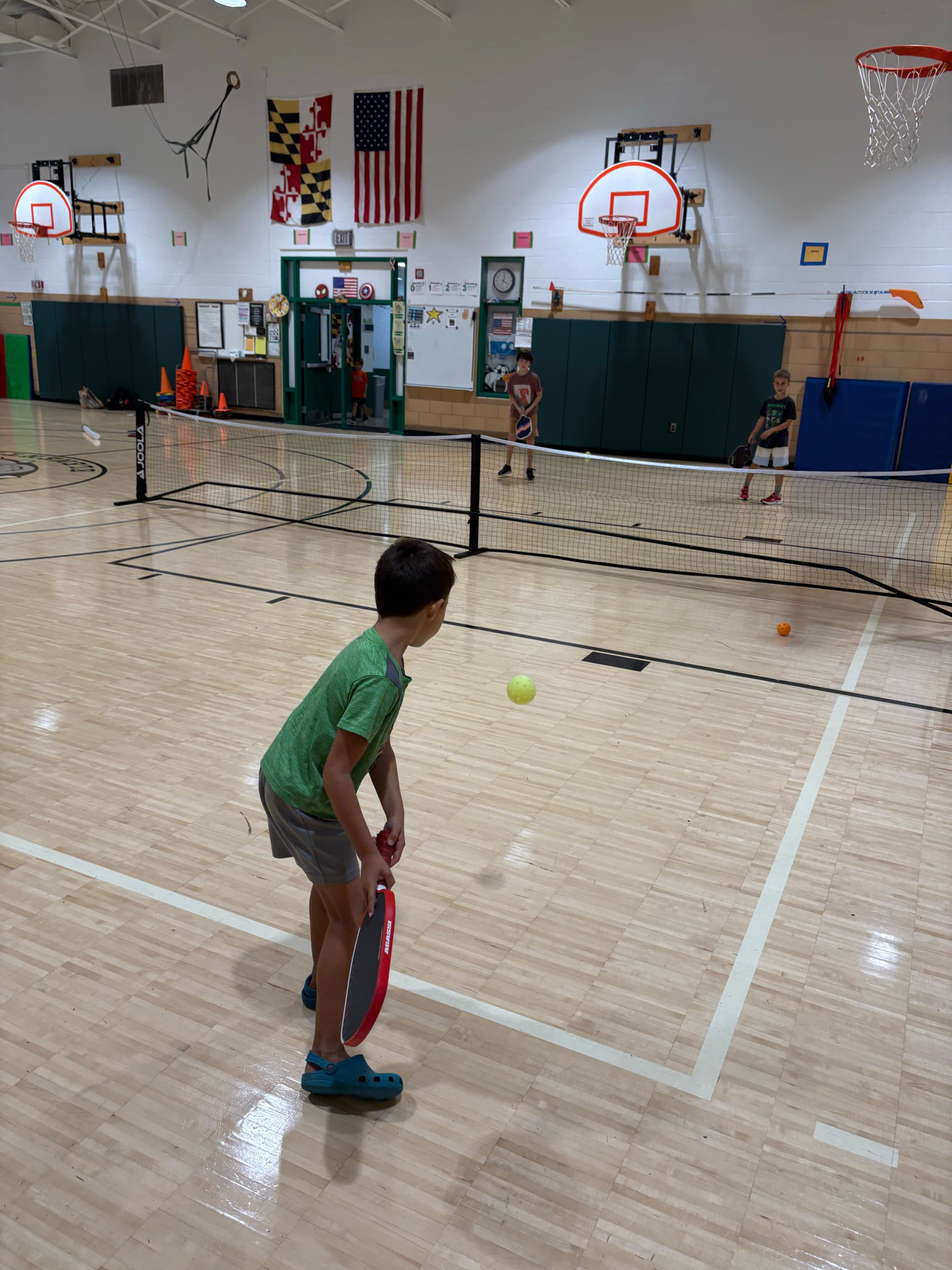 Young players playing doubles across a gym net